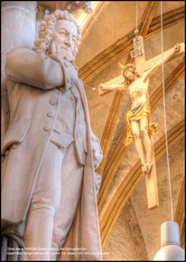 It is a photo of a Bach monument inside a church. In the background the is Jesus on the cross. The atmosphere is a warm yellow tone.