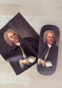 On the right is a glasses case, on the left is a glasses cleaning cloth. Both are on a neutral background. Everything is in very dark brown colors: It is the famous Haussmann portrait of J.S. Bach on both items in the Bach Shop.