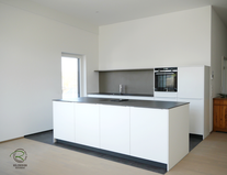 Kücheninsel in weiß mit Keramik-Neolith Arbeitsplatte mit Highboard für Kühl-Gefirrschrank u. Backofen mit brauner, indirekt beleuchteter Nischenrückwand u. Aluminium Griffleiste auf der Front u. flächenbündiger Induktion-Muldenlüfter Siemens