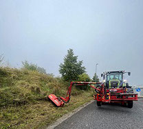 Ein Trecker mit einer Mulchvorrichtung bearbeitet Straßenränder.