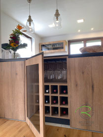 Halbinsel Küche mit Glasvitrine Weingläser und Flaschen integriert Schreinerküche in Tuttlingen in Eiche-Holzdekor und schwarz, mit Kochinsel und Vitrine mit Holzrahmen und rauchgrauem Glas für Weingläser und zur Lagerung von Weinflaschen