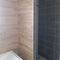 Création d'une salle de bain moderne et design avec du carrelage noir et du carrelage imitation parquet, bac à douche receveur design dans une petite salle de bain gain de place.