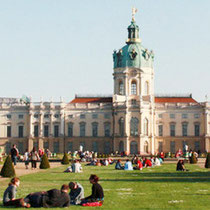 Menschen sitzen auf dem Rasen im Mai vor dem Schloss Charlottenburg. Foto: Helga Karl