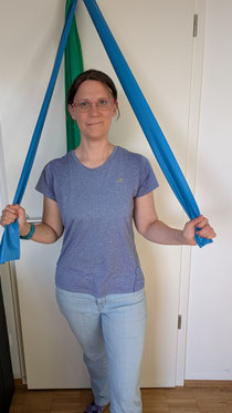 Foto von Stefanie- Kursleiterin- die freundlich mit einem Schritt nach vorne in die Kamera blickt und dabei zwei blaue Gymnastikbänder nach vorne zieht.