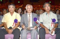 栄誉章を代理で受け、映像「65年の歩み」を見つめる(右から)広晃さん、憲一さん、栄さん=石垣市民会館、浜崎。
