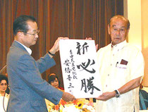 河村氏から安倍首相の為書きを受け取る仲井真氏(27日)