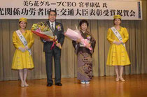 ミス八重山の2人から花束を贈られた宮平さん(中央)と妻の米子さん。関係者が大臣表彰の喜びを分かち合った=ホテルミヤヒラ
