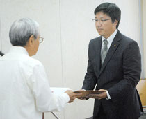 伊是名委員長から当選証書を受け取るトップ当選の平良氏=11日午前、市役所