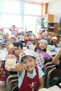 給食に登場したサッカーボール型のチーズに大喜びの八島小学校2年1組の児童=16日午後、同校2年1組の教室