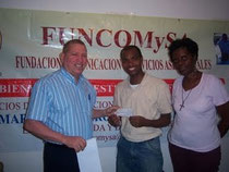 El comunicador Balbueno Medina entrega el cheque al padre Candelario Mejia Brito y la señora Dulce Figueroa quien canalizó la ayuda.