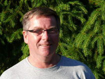 Ein lächelnder Mann mit kurzen grauen Haaren und einer Brille.