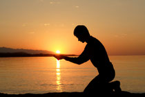 A man kneeling in worship at sunset on a beach