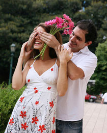 Young man surprises girlfriend with flowers while walking in flower garden.