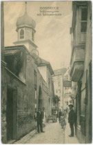 Handwerker der Schlossergasse im Bereich der Einmündung in den Westabschnitt der Seilergasse mit Glockenturm der ehemaligen Normalschulkapelle. Lichtdruck 9 x 14 cm; Impressum: Alois Nebl, Innsbruck um 1907.  Inv.-Nr. vu914ld00002