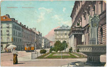 Dame in Tagestoilette beim Landesmuseum Ferdinandeum mit einem von zwei Zierbrunnen in Innsbruck, Museumstraße 15. Photochromdruck 9 x 14 cm; Impressum: K(arl). Redlich, Innsbruck 1910-11.  Inv.-Nr. vu914pcd00331