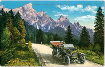 Automobil mit Chauffeur auf der Rollepassstraße vor der Palagruppe mit Cimon della Pala (3.184m) in den Dolomiten. Photochromdruck 9x14cm; Impressum: Joh(ann). F(ilibert). Amonn, Bozen um 1910.  Inv.-Nr. vu914pcd00211