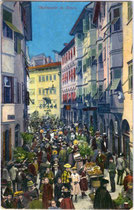 Buntes Markttreiben am Obstplatz in der Altstadt von Bozen, Südtirol. Photochromdruck 9 x 14 cm; Impressum: Joh(ann). F(ilibert). Amonn, Bozen 1915.  Inv.-Nr. vu914pcd00093