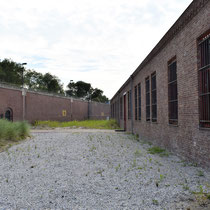 Buitenruimte met rechts het cellencomplex en links de buitenmuur met de toegangspoort op de oorspronkelijke locatie