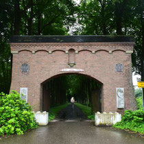03. Poort naar het hoofdgebouw met reliefs van wit natuursteen aan elke kant met daaronder een kleine gedenk plaquette