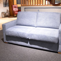 Graublaues Sofa auf einem Teppich, im Hintergrund ist ein Teil eines roten Sessels zu sehen.