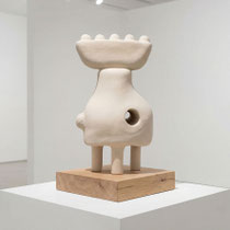 Ceramic sculpture by Alexandra Coutand, a textured organic form with a circular opening, displayed on a wooden base in a contemporary setting