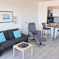 Wohnbereich der Ferienwohnung Nautilus Nr. 27 mit Sofa, Sessel und angrenzendem Essplatz
