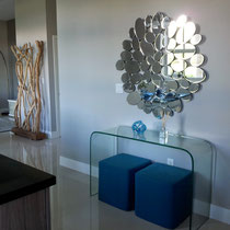 design project by Mia Home Trends featuring a modern glass console table and mirror with blue ottomans
