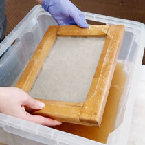 Eine Person hält ein Papierschöpfrahmen in der Hand im Workshop Papierschöpfen in Ganderkesee, Niedersachsen.