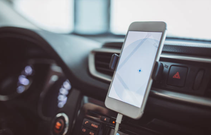 alt="Navigation auf dem Smartphone mit aktivierter Navigation App. Das Handy befindet sich im Auto neben dem Lenkrad"