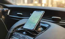 alt="Navigation auf dem Smartphone mit aktivierter Navigation App. Das Handy befindet sich im Auto neben dem Lenkrad"