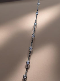 Delicate silver bracelet with several clear round-set stones against a softly lit neutral background. Minimalist and light-focused product photo.