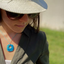 jeune feme portant champeau, saison estivale, haute décoleté mettant en avant un collier rond style donut bleu lagon