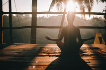 Jemand sitzt in Meditationshaltung in einem Baumhaus in den Tropen