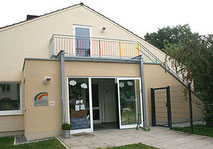 Eingangsbereich des Evangelischen Kindergartens 'Unter dem Regenbogen' in Hagen mit gläserner Eingangstür und Balkon.