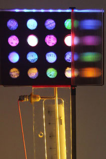 Assemblage light art sculpture consisting of a scientific instrument made of plexiglas, paper and wood with holes illuminated with LEDs from behind, refracted light created by lined plexiglas, and circles of old French checks which cover the holes.