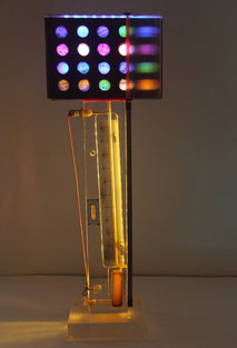 Assemblage light art sculpture consisting of a scientific instrument made of plexiglas, paper and wood with holes illuminated with LEDs from behind, refracted light created by lined plexiglas, and circles of old French checks which cover the holes.