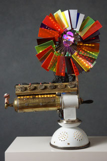 Assemblage light art sculpture made from a spaghetti strainer, a meat grinder, a chimney sweep brush, a water bottle, and watch parts. When the meat grinder is turned, LEDs behind the plexiglas are lit up, cause by the making of an electrical connection. 