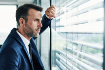 Manager schaut nachdenklich zum Bürofenster raus als Motivbild für Business-Coaching von Georgia Middel bei Burnout, Erschöpfung, Stress, Karriere