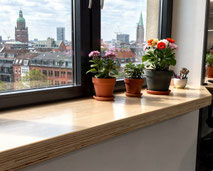Holzfensterbank aus Multiplex-Birke geölt oder mit Hartwachs behandelt - vor einem dunklen fensterrahmen, Blumentöpfe und Blick auf Hamburg