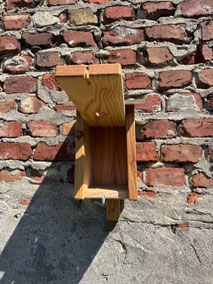 Geöffneter Nistkasten an Ziegelwand. Aus Holz gefertigt mit einer Ringschraube zum verschließen.