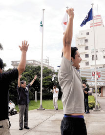 北上市の旗を掲揚後、万歳する漢那副市長(中央左)と職員ら=28日午前石垣市役所