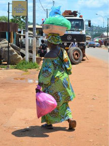 Femme africain habillée en tissu wax vert portant sur la tête une bassine