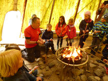Kinder und ein Erwachseber beim Stockbrot machen am Lagerfeuer im Tipi.
