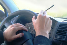 Hände am Steuerrad beim Auto fahren mit CBD Joint in der Hand