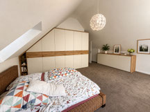 Maßgefertigter Einbauschrank unter der Dachschräge im Schlafzimmer in Rottweil mit weißen Fronten, horizontalem Eiche-Dekorstreifen und passender Kommode nach Maß.