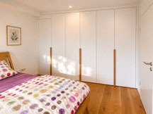 Maßgefertigter Kleiderschrank nach Maß im Schlafzimmer in Rottweil mit weißen Fronten, durchgehenden Eichen Holzgriffen und raumhoher Ausführung vom Schreiner.