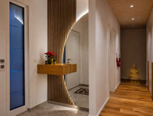 Halbrunder Flurspiegel mit indirekter LED-Beleuchtung, schwebendem Eiche-Sideboard und Holzlamellen im Eingangsbereich eines Einfamilienhauses in Spaichingen