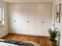 Maßgefertigter Kleiderschrank im weißen Landhausstil mit klassischen Rahmenfronten nach Engen, schwarzen Möbelknöpfen und individueller Inneneinteilung für ein Schlafzimmer – gefertigt von Holzdesign Rapp.