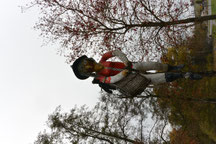 Foto von einer großen hölzernen Hexenfigur mit Hut, roter Jacke und weißer Hose, die auf einem Besen mittig auf den Betrachter zuzufliegen scheint