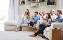 Familie zuhause gemeinsam beim Fernsehen vorm TV-Gerät beim Film oder Video schauen bei Treffen mit Freunden und Bekannten